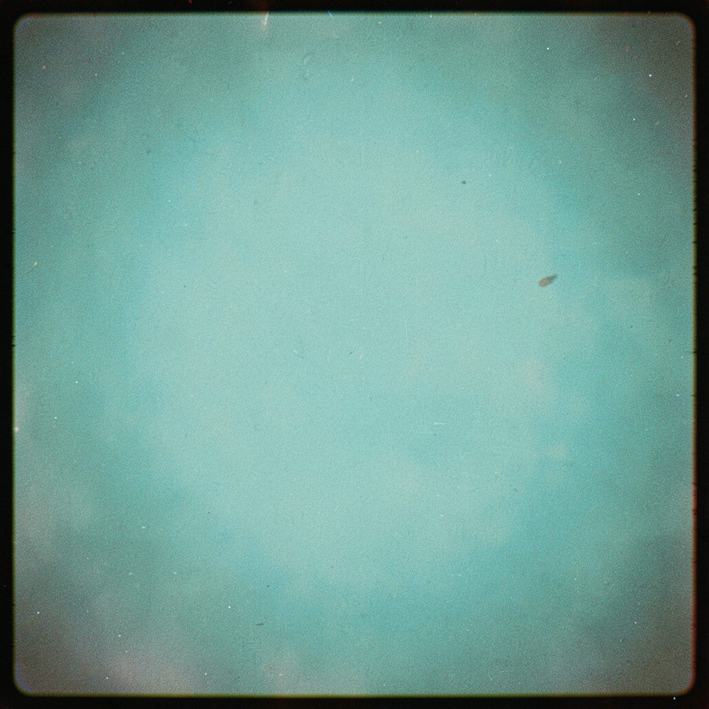 A grainy film photograph of a fly rod bent against a moody overcast sky, deep teal water below, the angler's silhouette barely visible in the frame.